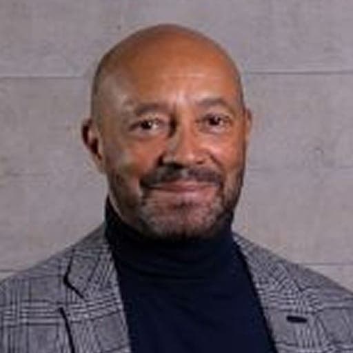 Sir Damon Buffini, Chair of the Queen Elizabeth Trust, smiling at the camera in a studio portrait.